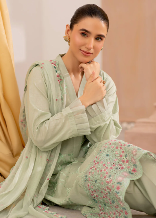 Woman wearing a light green traditional outfit with floral patterns indoors.