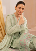 Woman wearing a light green traditional outfit with floral patterns indoors.
