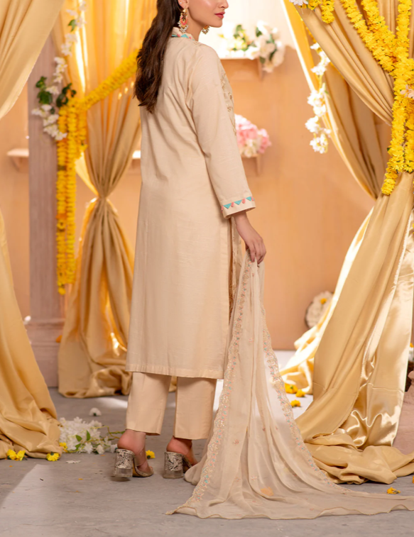 Woman in a beige traditional outfit standing in a decorated indoor setting with yellow and beige drapes.