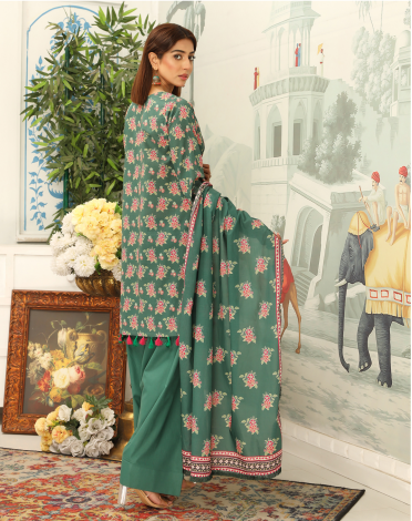 Woman in a green floral saree standing in a decorated room with flowers and a painting.